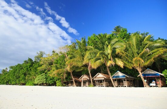 Indonesien, Moluccas: White sandy beach with palm trees and wooden houses