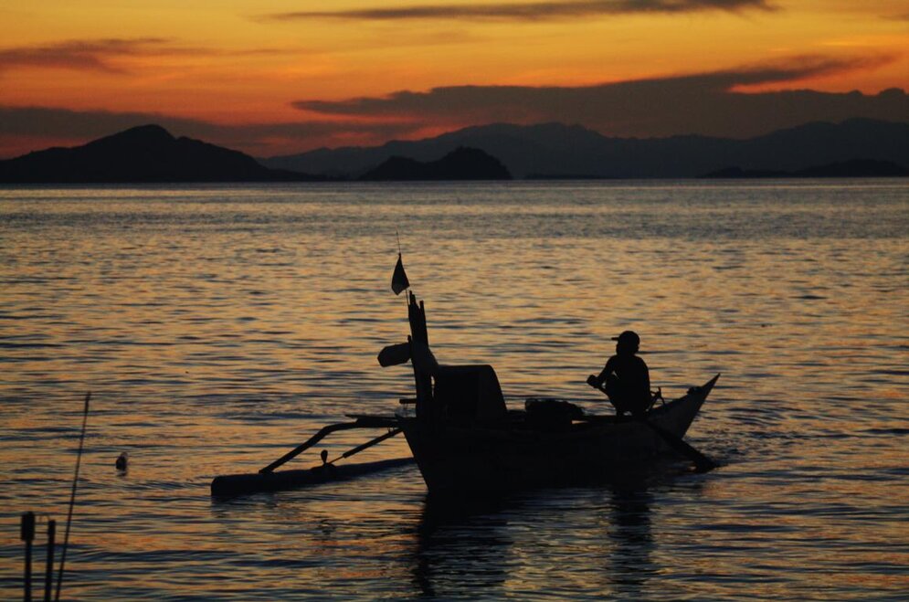 Indonesische Insel Flores: Mann in kleinem Holzboot bei Sonnenuntergang