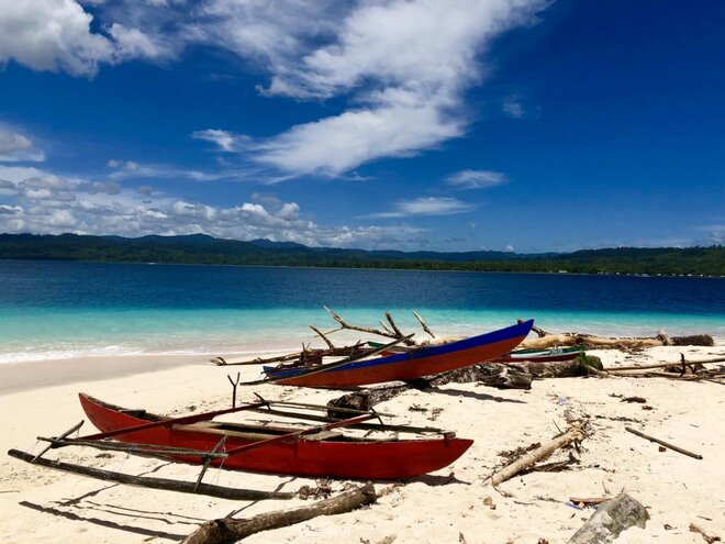 Two red wooden boats on white sandy beach of Morotai, Moluccas, Spice Islands